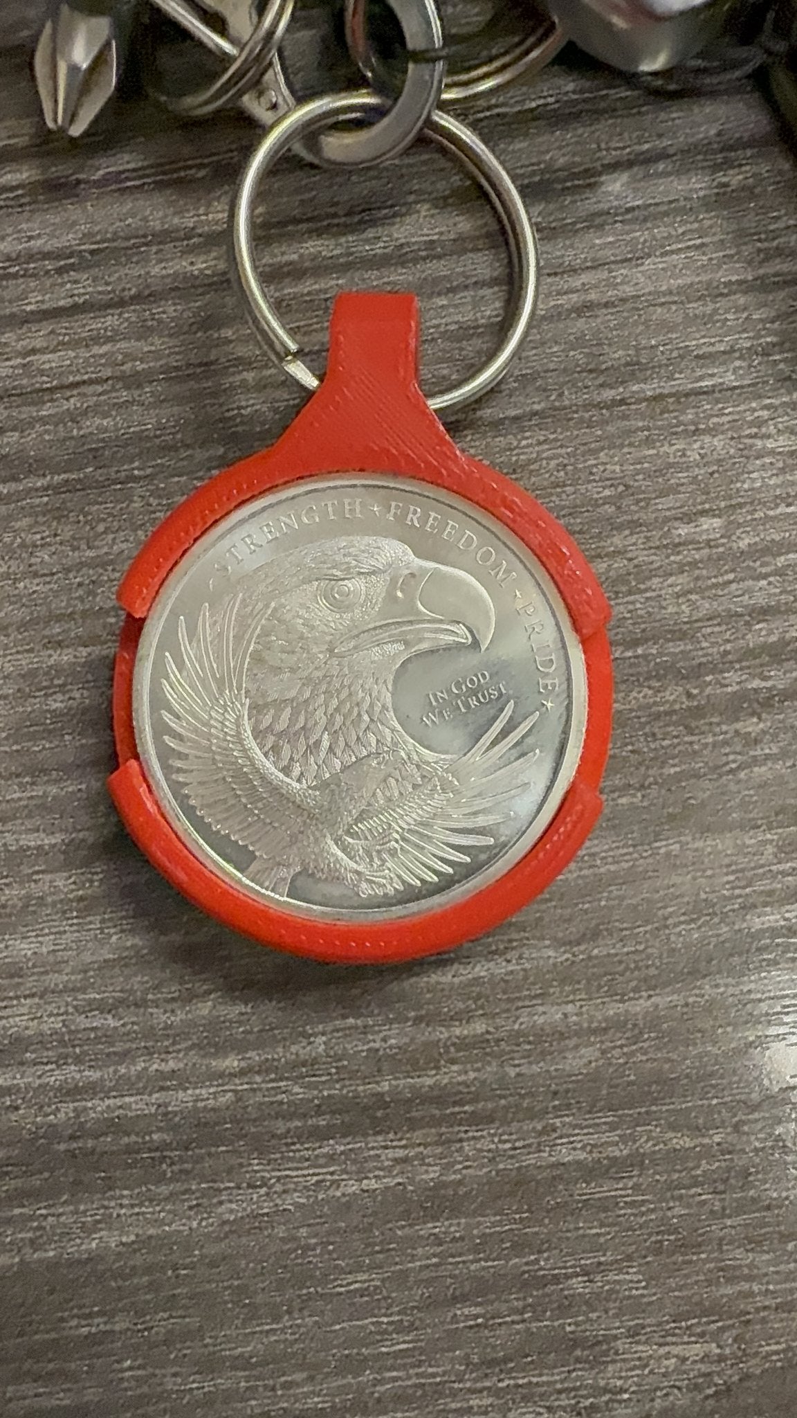 Red 3D printed Coin AirTag Hiding Keychain holding a 1 oz silver eagle round, close up