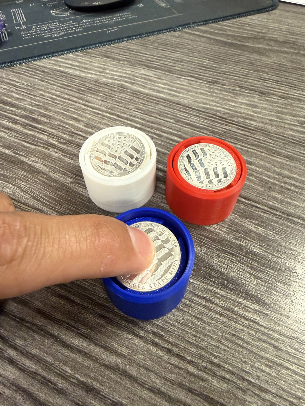 A thumb pressing the silver round on a blue Silver Coin Fidget Clicker to click it