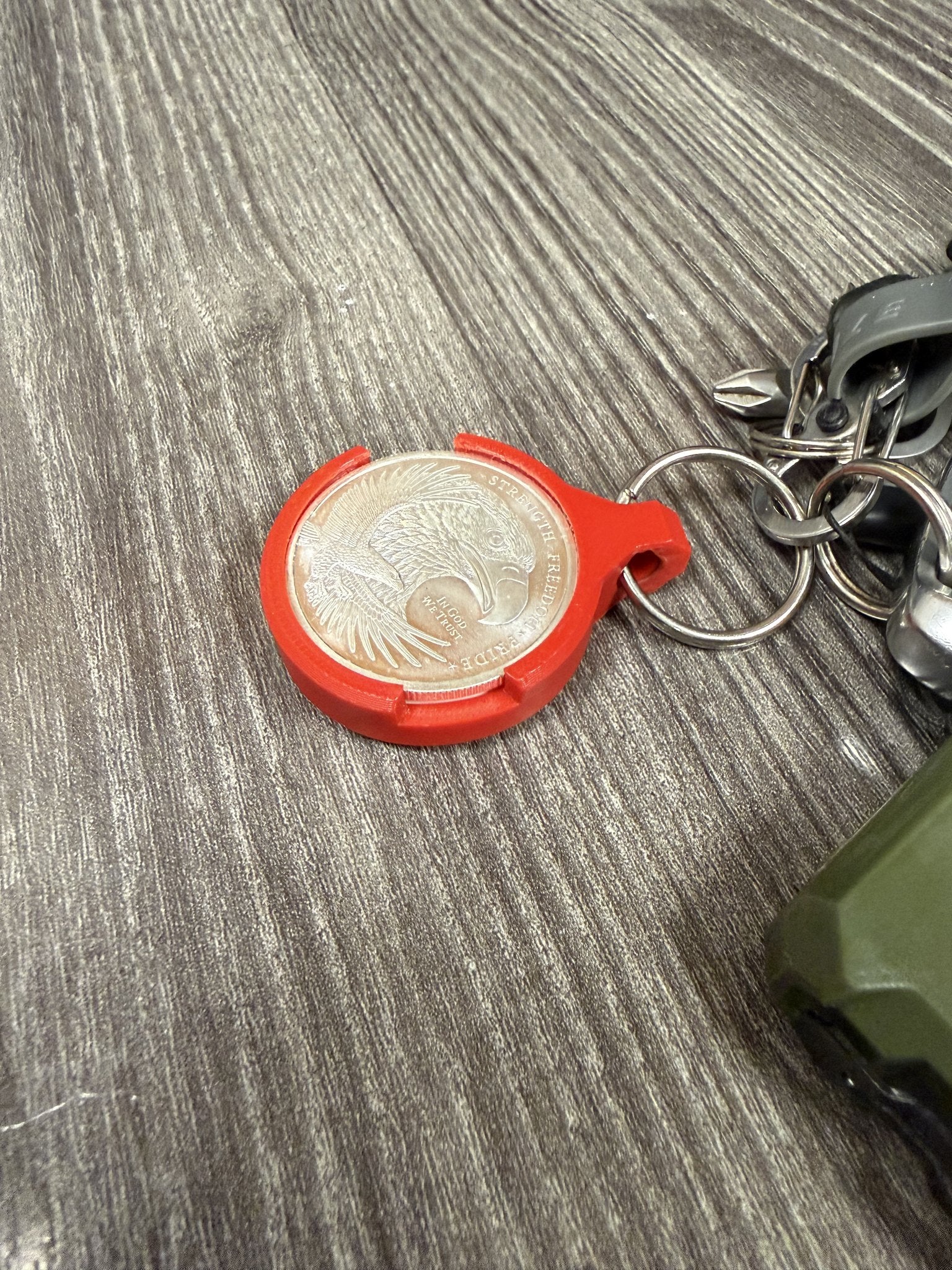 Red coin keychain hanging from a split ring, showing the integrated keyring loop