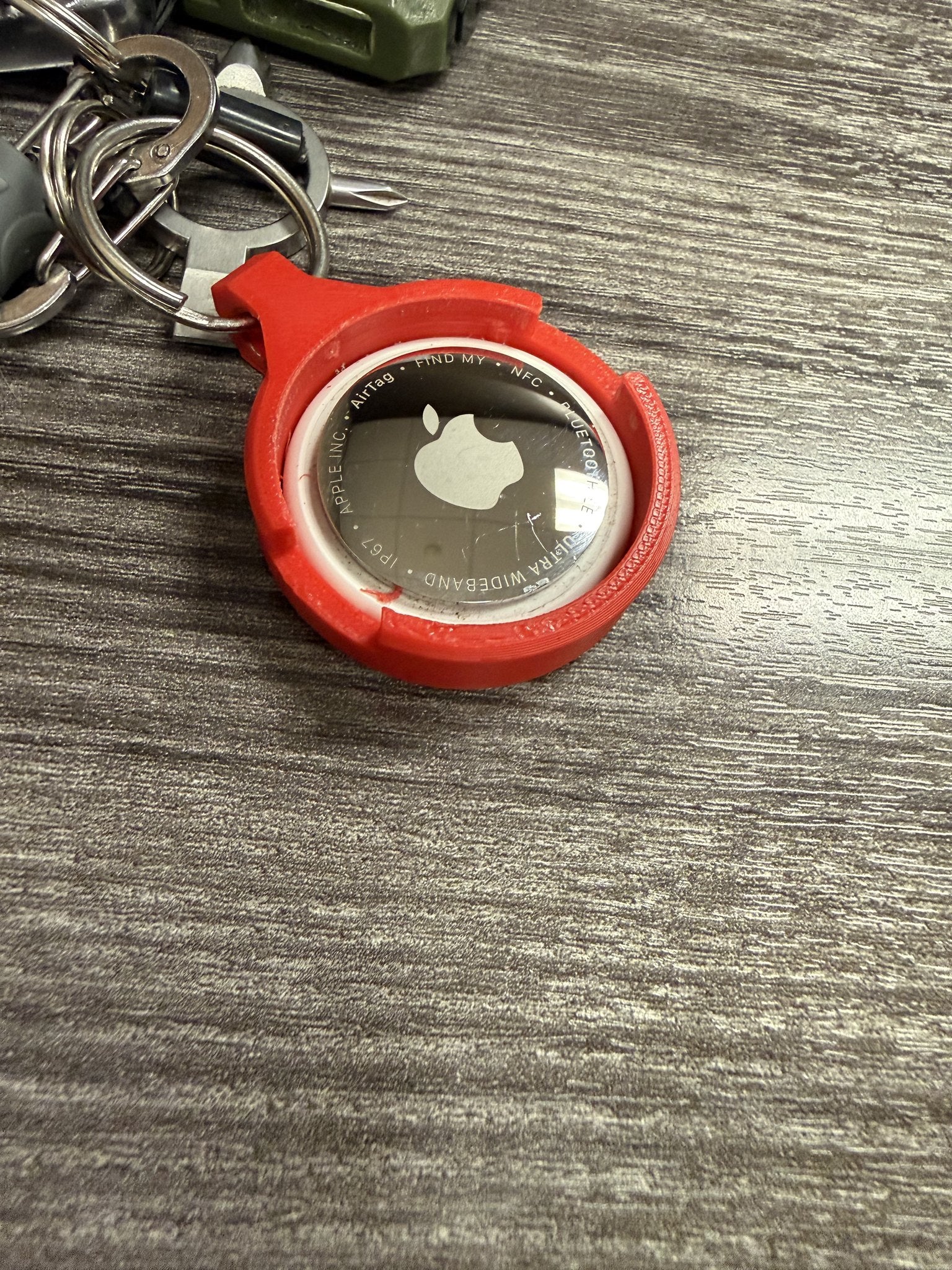 Apple AirTag seated in the back of the red Coin AirTag Hiding Keychain, showing how the tracker mounts behind the coin